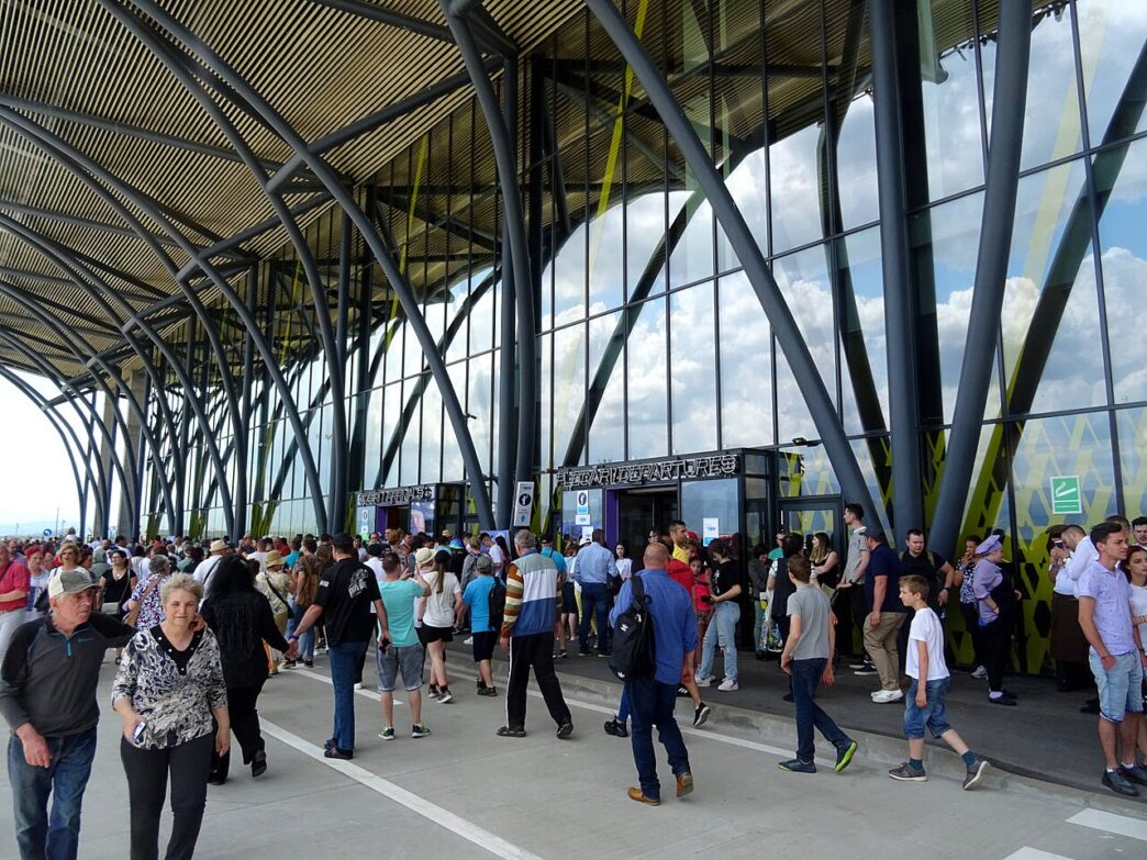 Pasageri în fața terminalului Aeroportului Internațional Brașov-Ghimbav, sub structura metalică ramificată a fațadei