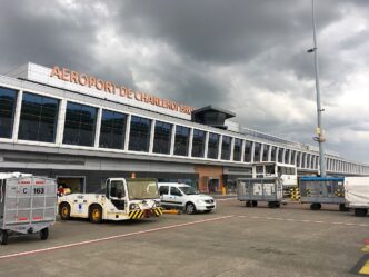 Clădirea terminalului 1 al aeroportului Bruxelles Charleroi, văzută de pe platformă, cu vehicule de handling și cărucioare de bagaje