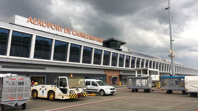 Clădirea terminalului 1 al aeroportului Bruxelles Charleroi, văzută de pe platformă, cu vehicule de handling și cărucioare de bagaje