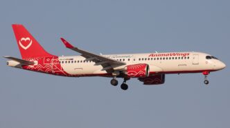 Aeronavă Airbus A220-300 în livrea roșu cu alb, cu trenul de aterizare coborât, pe cer senin
