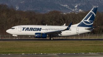 Avion Boeing 737-700 al TAROM, în livrea albastru cu alb, rulează pe pista unui aeroport, cu dealuri împădurite în fundal