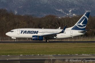 Avion Boeing 737-700 al TAROM, în livrea albastru cu alb, rulează pe pista unui aeroport, cu dealuri împădurite în fundal