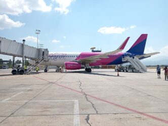 Avion Airbus A320 în culorile Wizz Air pe platformă, cu scări mobile la ușile din față și din spate, personal de sol și câțiva pasageri, într-o zi senină